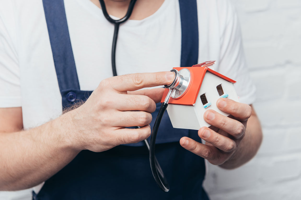 man holding a stethoscope up to a model house
