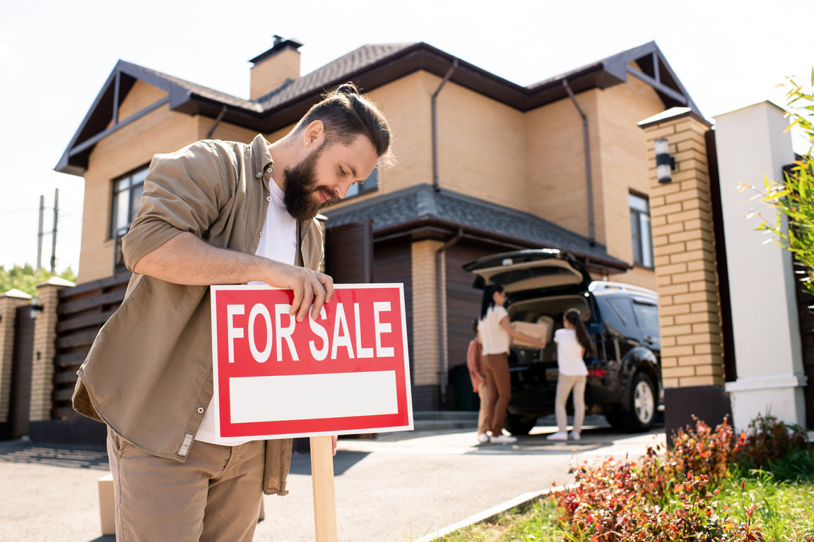 man placing for sale sign in front of home